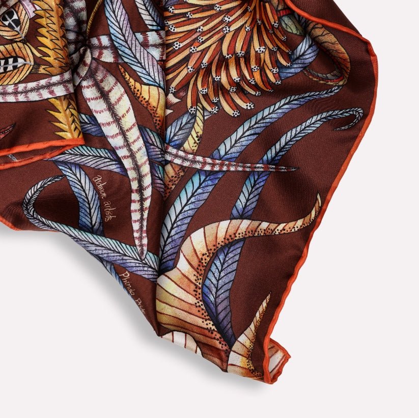 A portion of the scarf's flowing silk fabric, folded to display the hand-rolled edges and intricate details of the design.