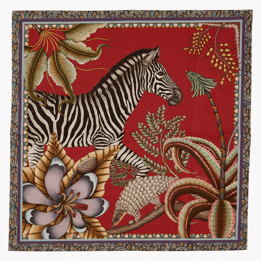 A full view of the Ardmore Thanda Stripe Napkin in Royal Red, displaying its detailed artwork featuring zebras, pangolins, and botanical elements framed within an ornate border.