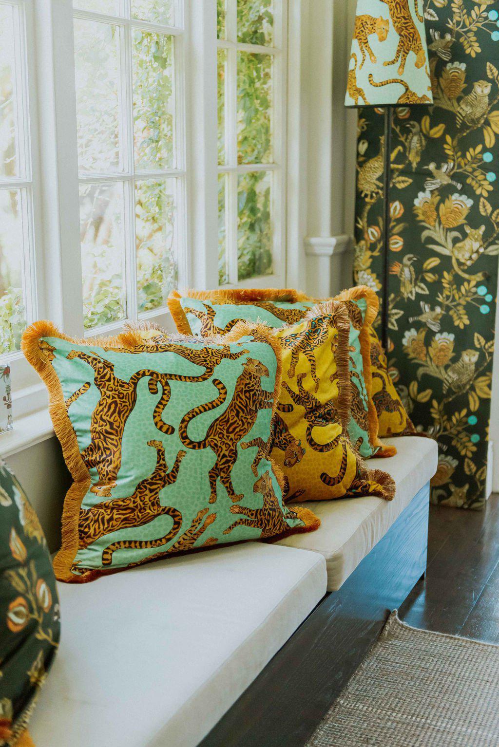 Indoor display of the Cheetah Kings Jade velvet cushion cover, styled on a sofa in a bright, elegant room with complementary decor and botanical-themed wallpaper.