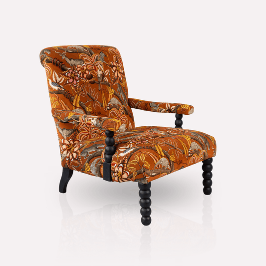 Ardmore Kudu Pod Chair in Pangolin Park Rust Velvet, featuring bold burnt-orange fabric with intricate African-inspired patterns, plush cushioning, and black wooden legs.
