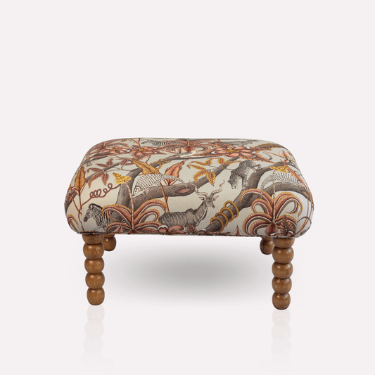 Ardmore Kudu Pod Ottoman in Pangolin Park Plum Linen, featuring intricate African-inspired patterns with turned wooden legs.