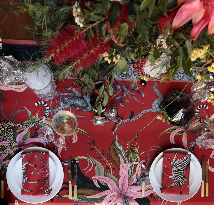 A lavishly set dining table featuring the Leopard Lily Tablecloth in Royal Red, decorated with red floral centrepieces and candlelit accents.