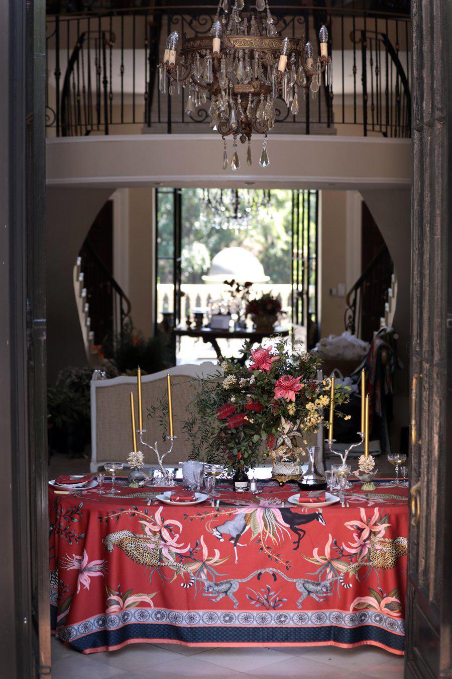 The Leopard Lily Tablecloth in Royal Red used in a sophisticated indoor setting, draped over a dining table in a beautifully lit space.