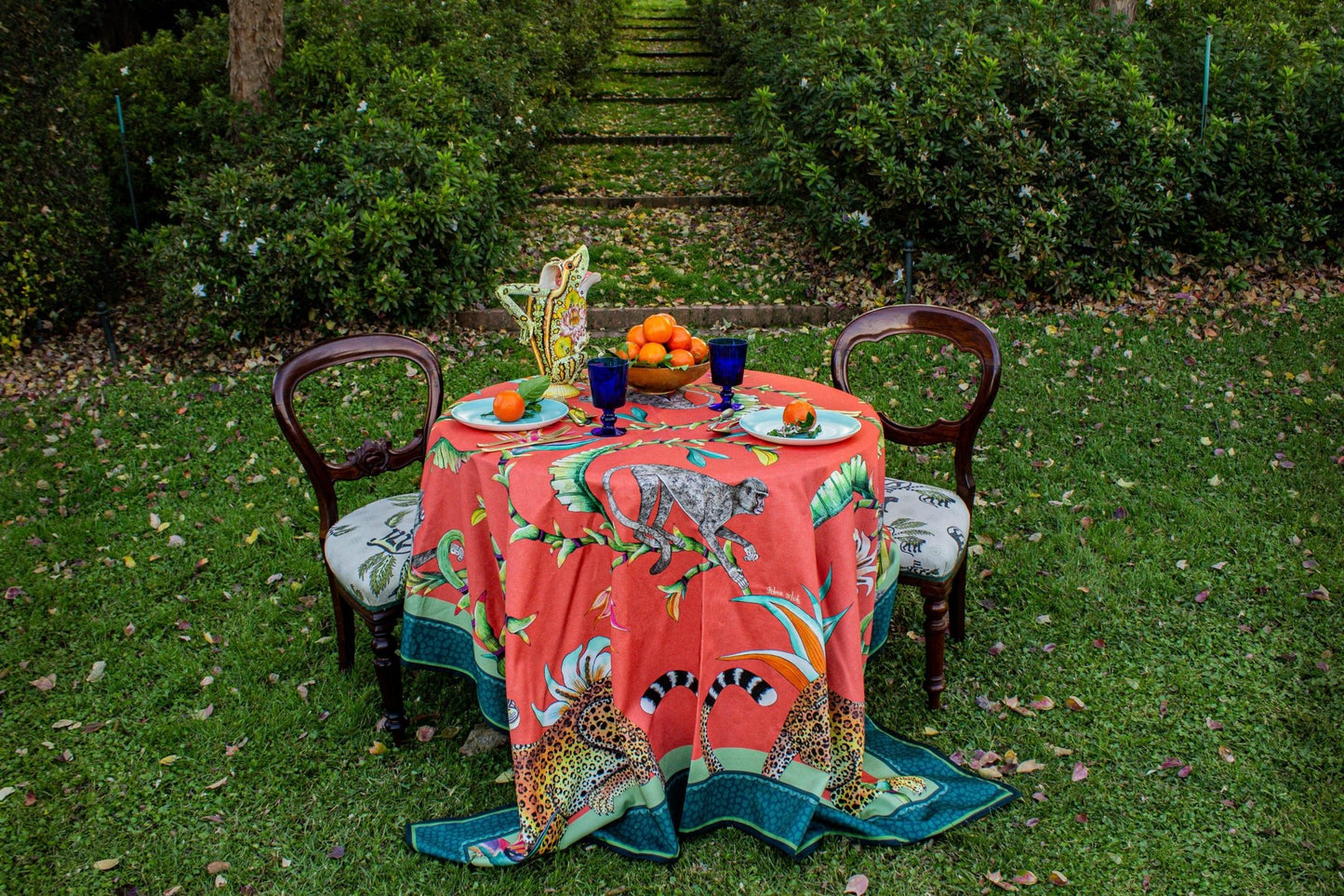 The Monkey Paradise Square Tablecloth elegantly draped over a table in an outdoor environment, blending nature with artistry.