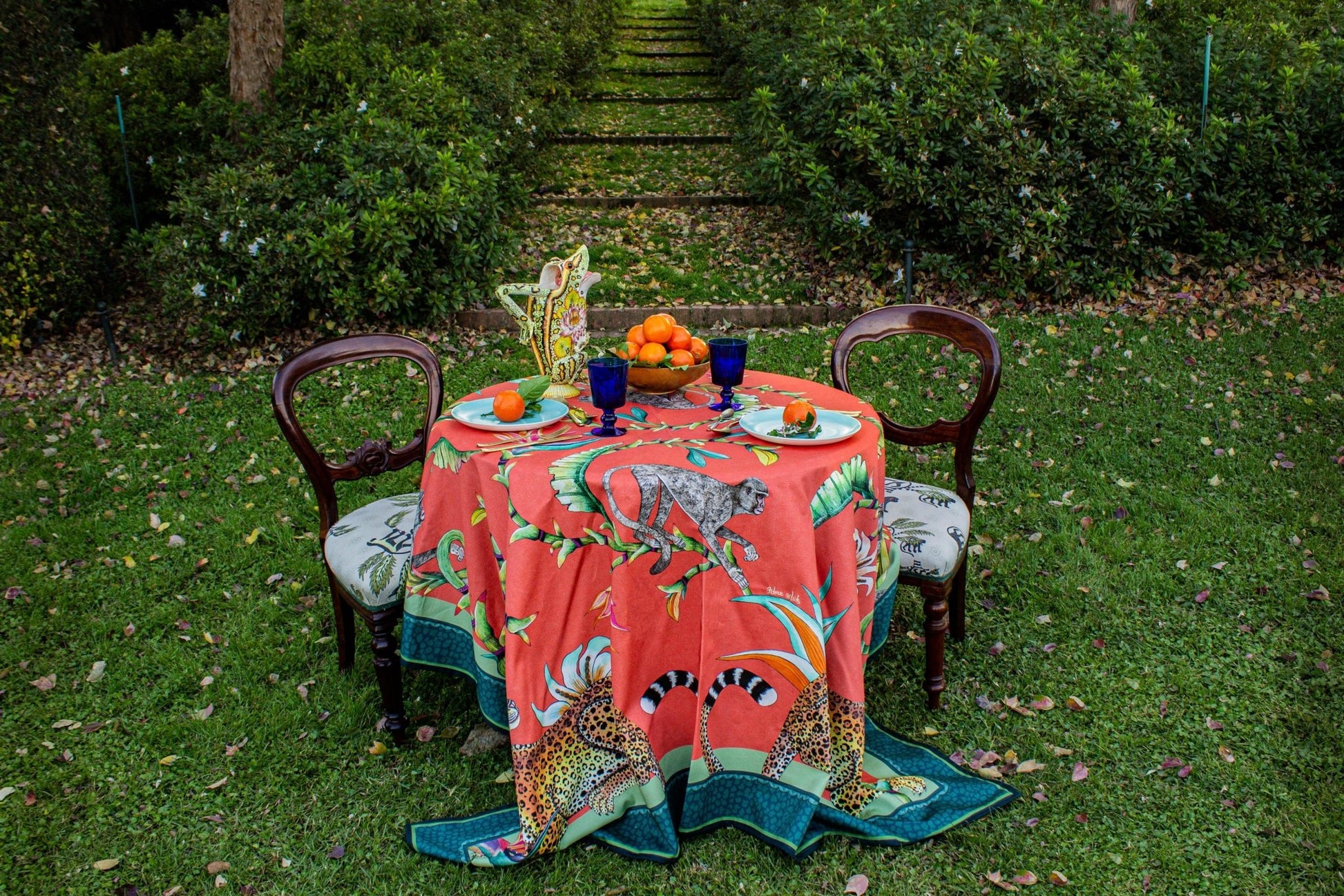 The Monkey Paradise Square Tablecloth elegantly draped over a table in an outdoor environment, blending nature with artistry.