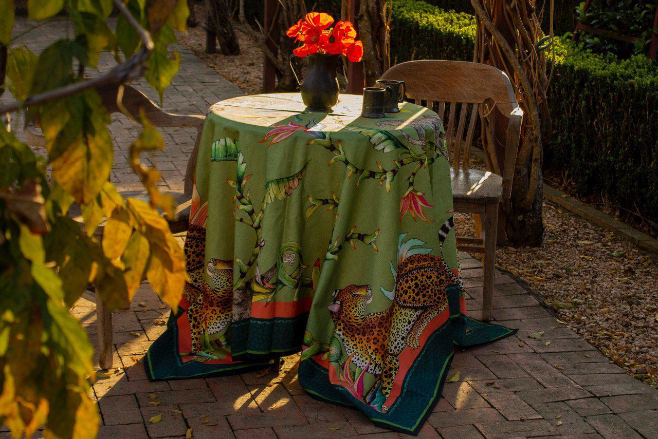 A table set outdoors with the Monkey Paradise Square Tablecloth in green, surrounded by lush greenery.