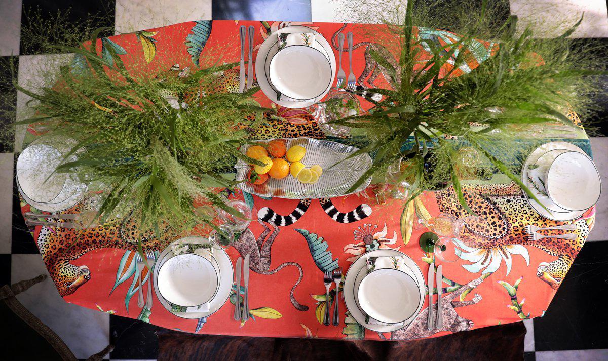 A beautifully styled outdoor dining table featuring the Monkey Paradise Tablecloth in Coral, with matching tableware and glassware.