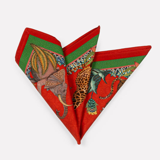 A pair of Ardmore Sabie Forest Napkins in Royal Red, folded into a fan shape, showcasing a vibrant red background with lush green foliage and a detailed leopard illustration.