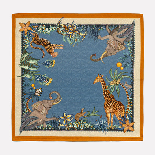 A single Ardmore Design Sabie Forest napkin laid flat, showcasing its tanzanite blue background with detailed African wildlife and botanical motifs in gold and orange.