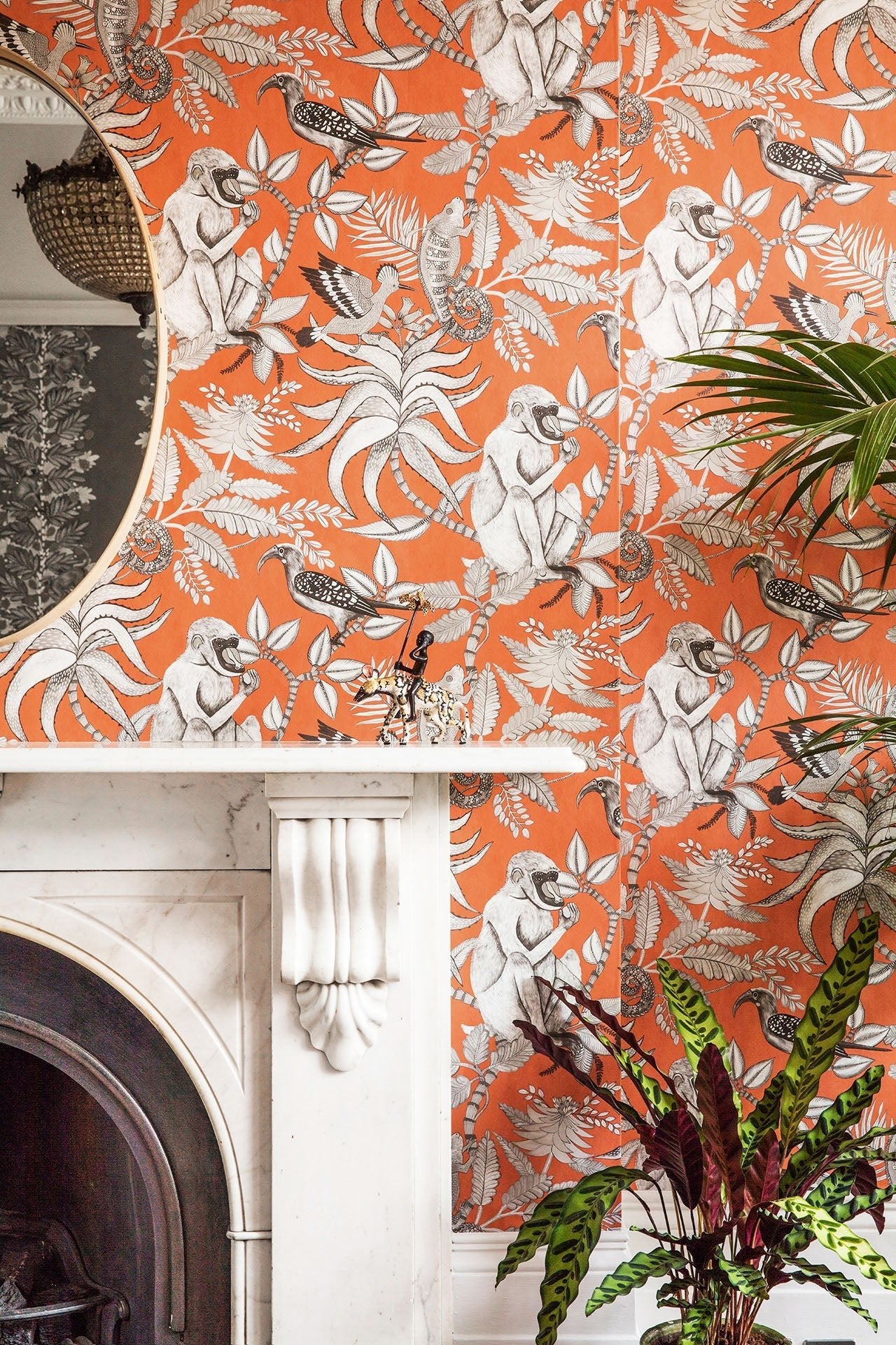 A chic interior with a white fireplace, contrasted by vibrant orange Savuti wallpaper decorated with leopards and lush foliage.