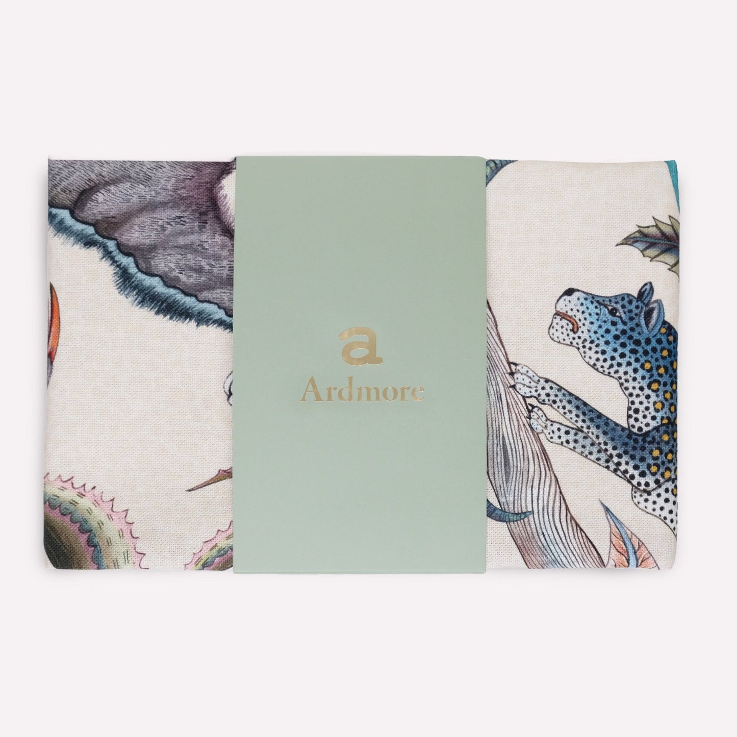 A tea towel in its original packaging, displaying the vibrant mix of animals and tropical flora in a sophisticated blue-toned theme.