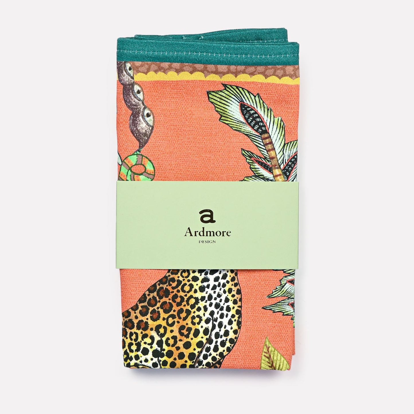 A neatly folded Ardmore Leopard Napkin in Coral, wrapped in its original branded packaging, displaying the fine craftsmanship and artistic elegance.
