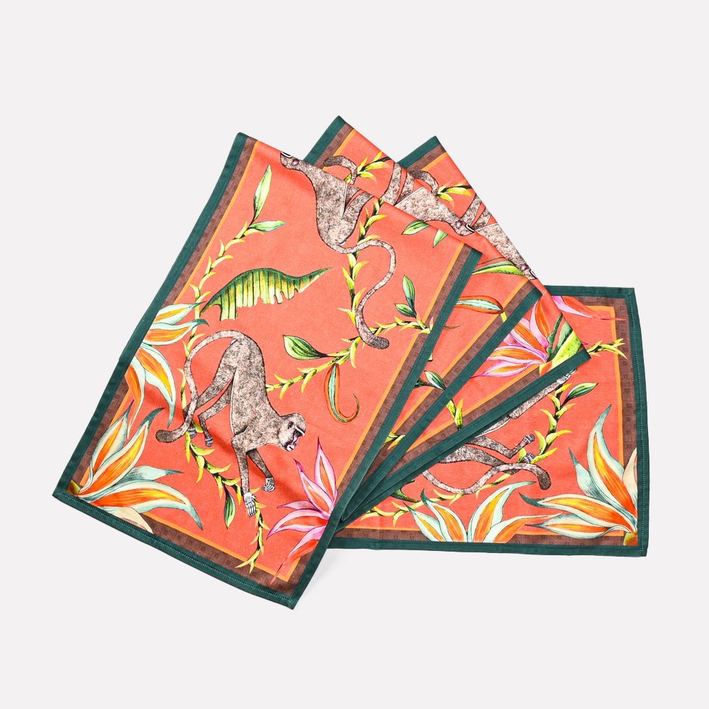 A set of Ardmore's Monkey Paradise table runners in a vibrant Coral hue, featuring intricate artwork of leopards, jackals, and lush tropical foliage.