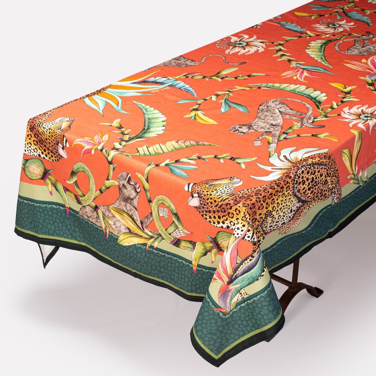 The Monkey Paradise Tablecloth in Coral elegantly draped over a table, showcasing its intricate design and contrasting green border.