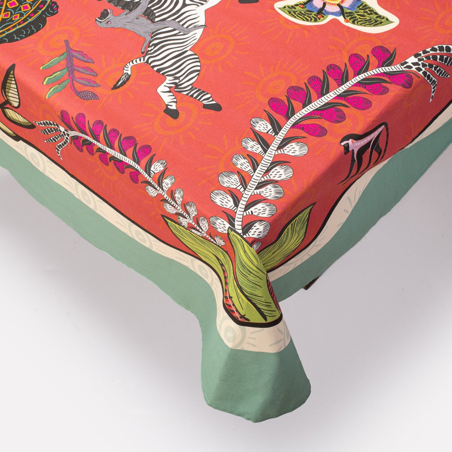 A detailed shot of the tablecloth’s corner, showing the luxurious fabric drape, intricate design, and contrast between the red main body and the green border.