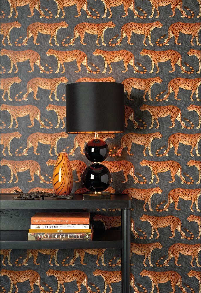 A striking burnt-orange wallpaper featuring a parade of leopards, paired with a black lamp and a luxury Ardmore sculpture.