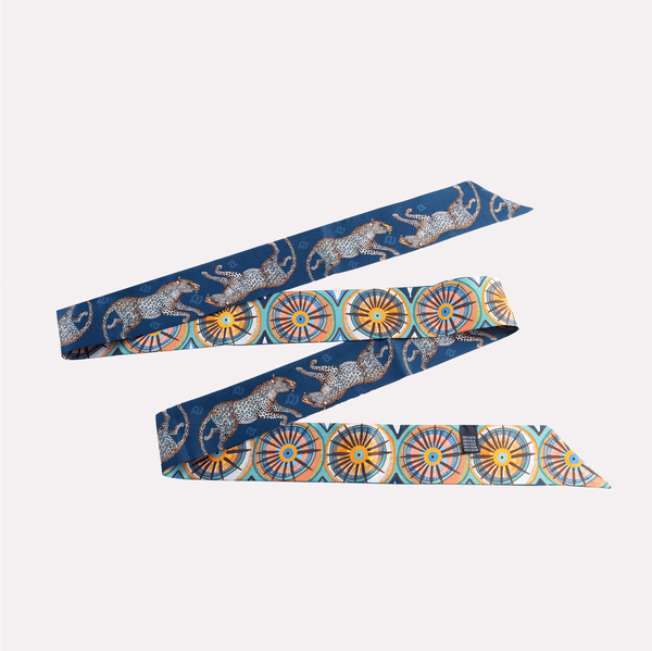 A long, double-sided silk twilly featuring intricate Amasumpa African prints and leopards against a rich tanzanite blue background.