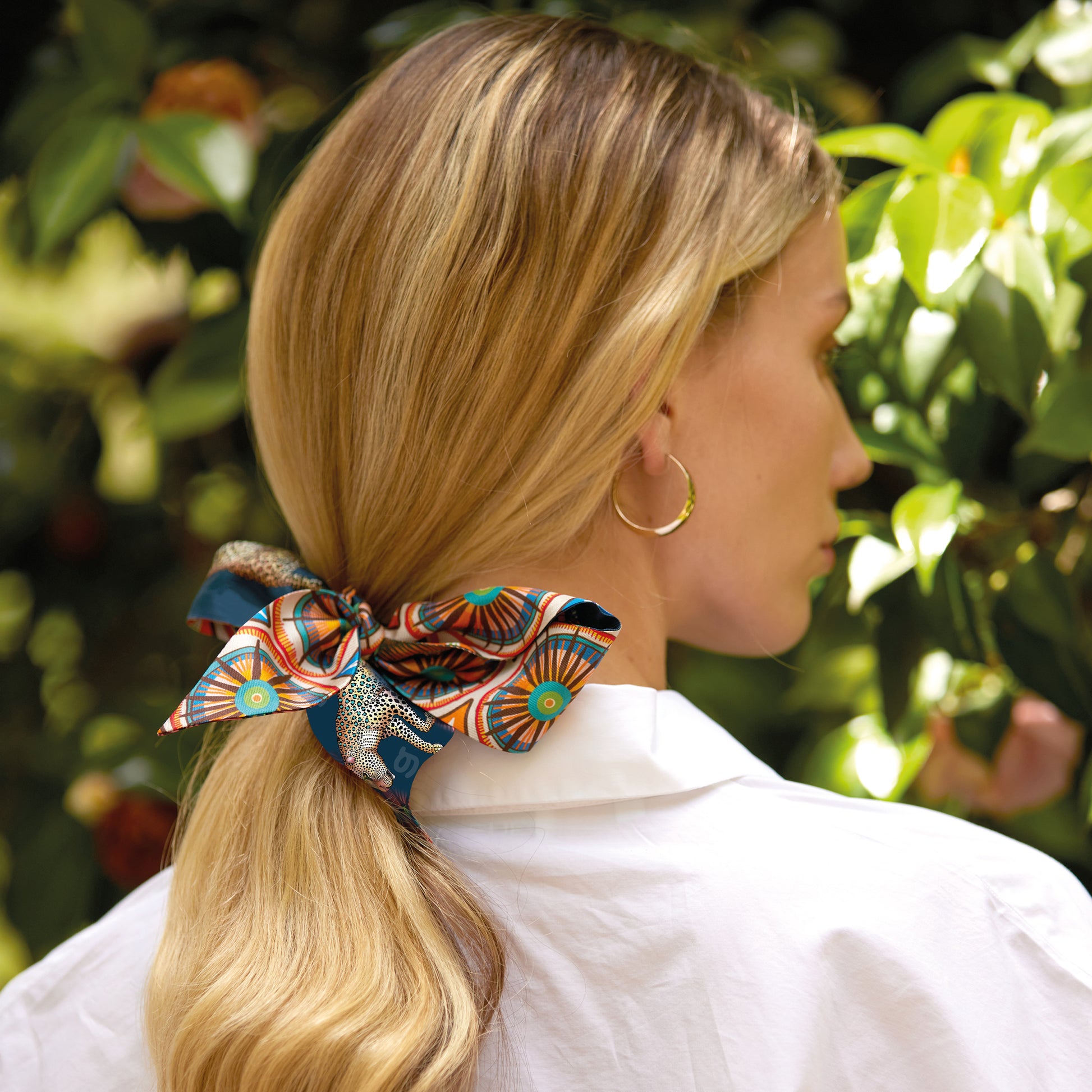A woman with blonde hair wears the twilly elegantly tied as a hair accessory, showcasing its versatility.