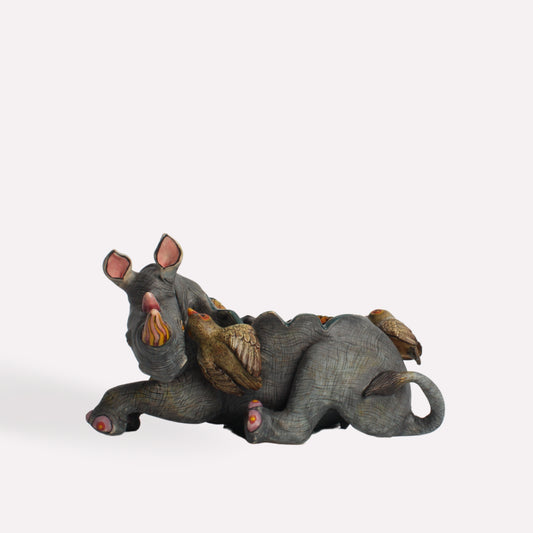 A sculptural bowl featuring a reclining rhino with intricate hand-painted details. The rhino’s textured skin and expressive features bring realism, while lush foliage elements adorn its back.
