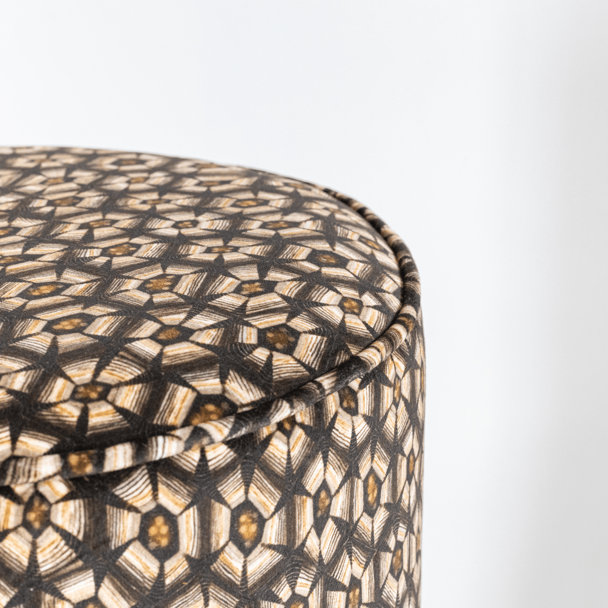 A closer look at the pouffe’s upholstery, showing the detailed craftsmanship and the contrast between the silver-patterned velvet and the brass base.
