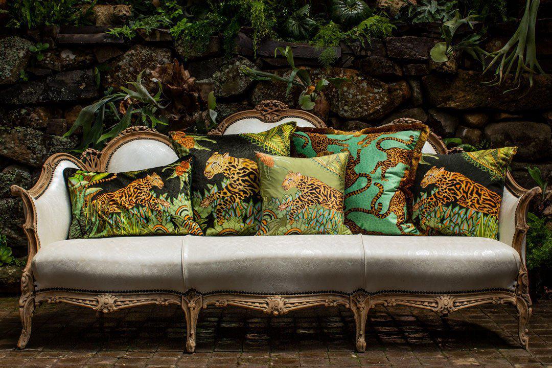 Outdoor setting featuring a vintage cream sofa adorned with Ardmore Design's Cheetah Kings Jade velvet cushions, highlighting their vibrant colours and luxurious design in a lush garden backdrop.
