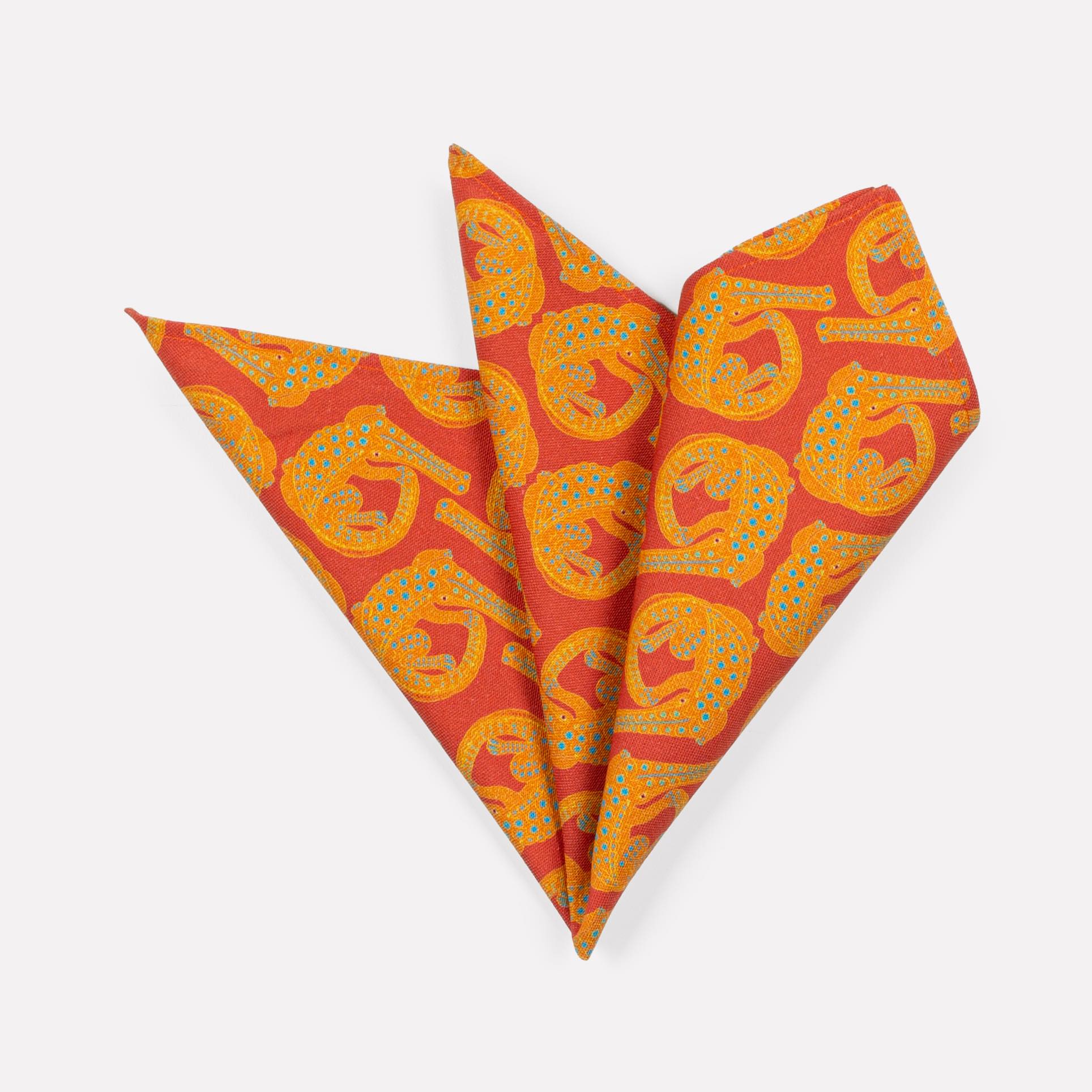 A pair of Ardmore Croco napkins in Sunset, elegantly folded into a fan shape to highlight the bold reptilian motif and rich sunset-toned fabric.
