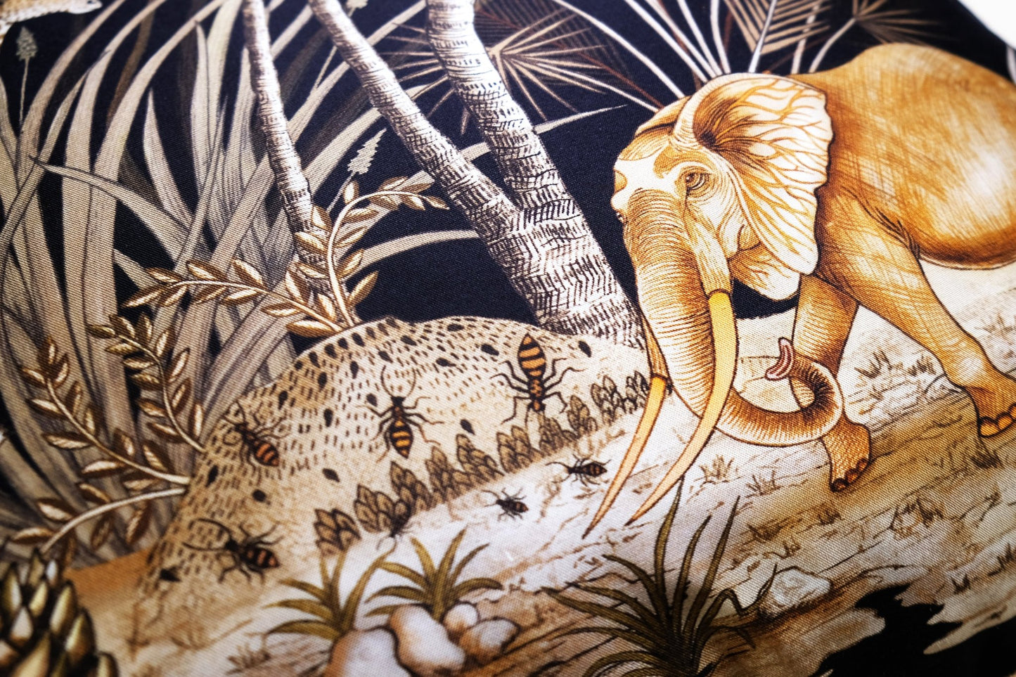 A detailed view of an elephant resting among tall grass and trees, highlighting the rich golden embroidery against the black background.