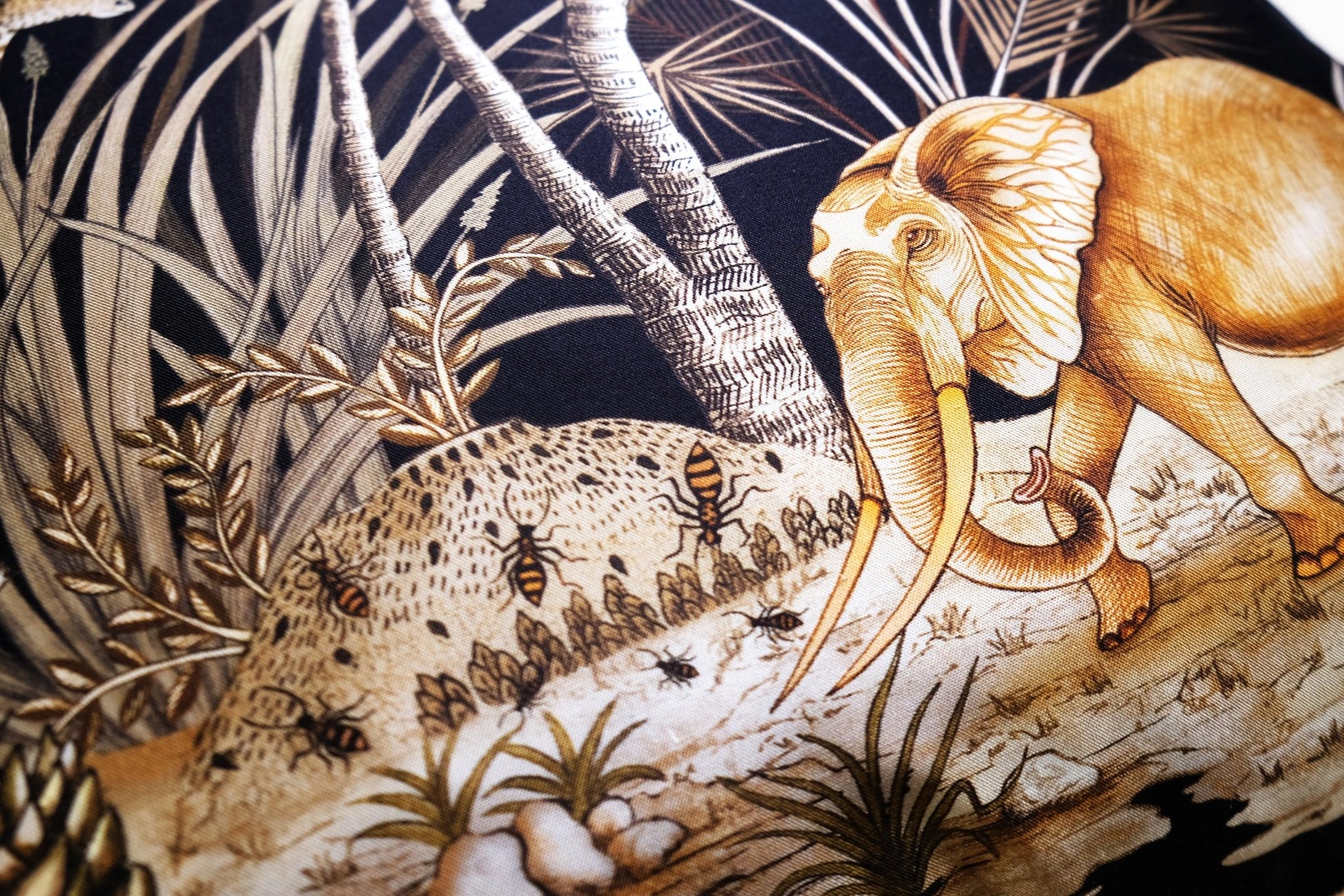 A detailed view of an elephant resting among tall grass and trees, highlighting the rich golden embroidery against the black background.