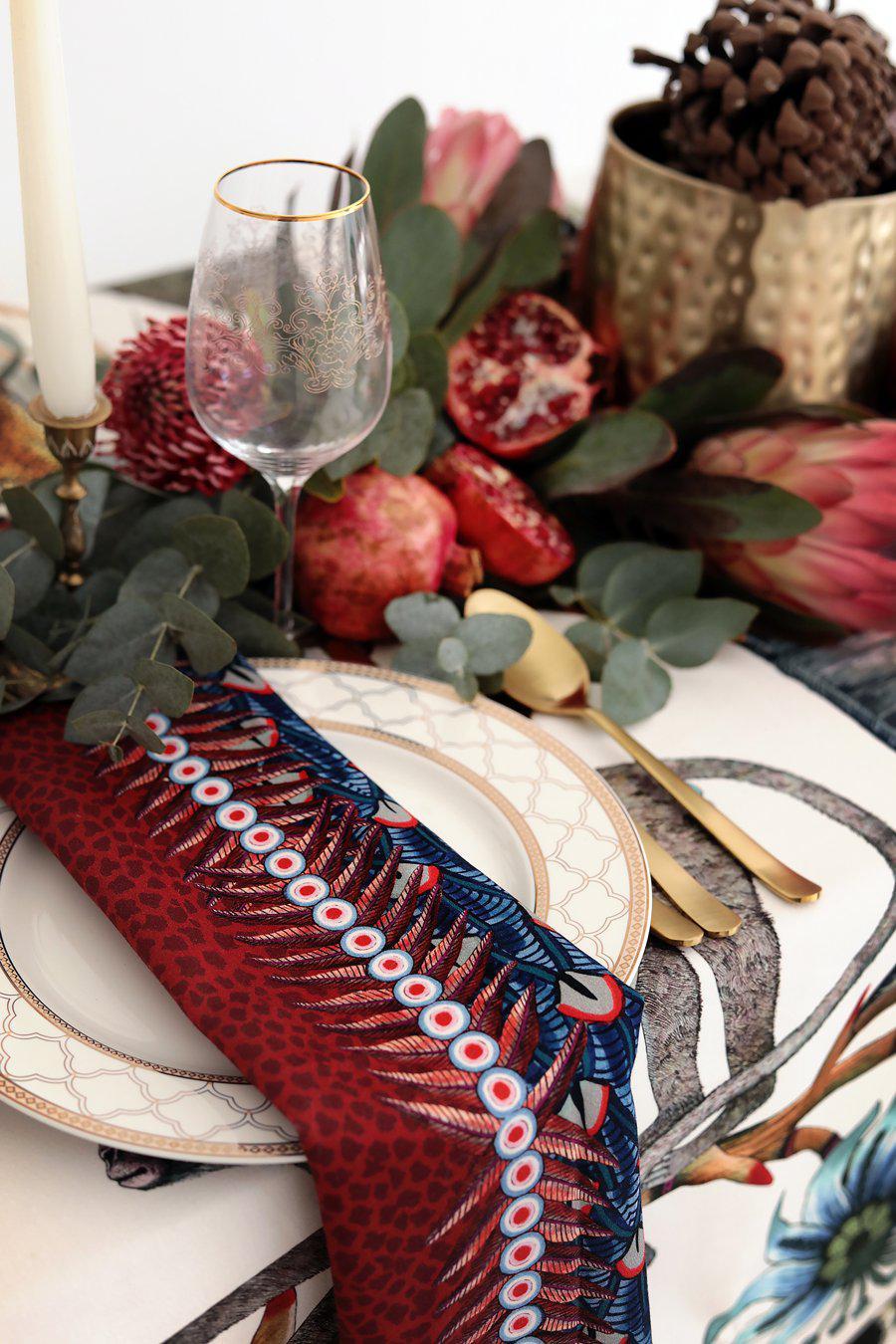 A festive table setting featuring the Ardmore Feather napkin in Royal Red, elegantly placed among tableware and decorations for a luxurious dining experience.