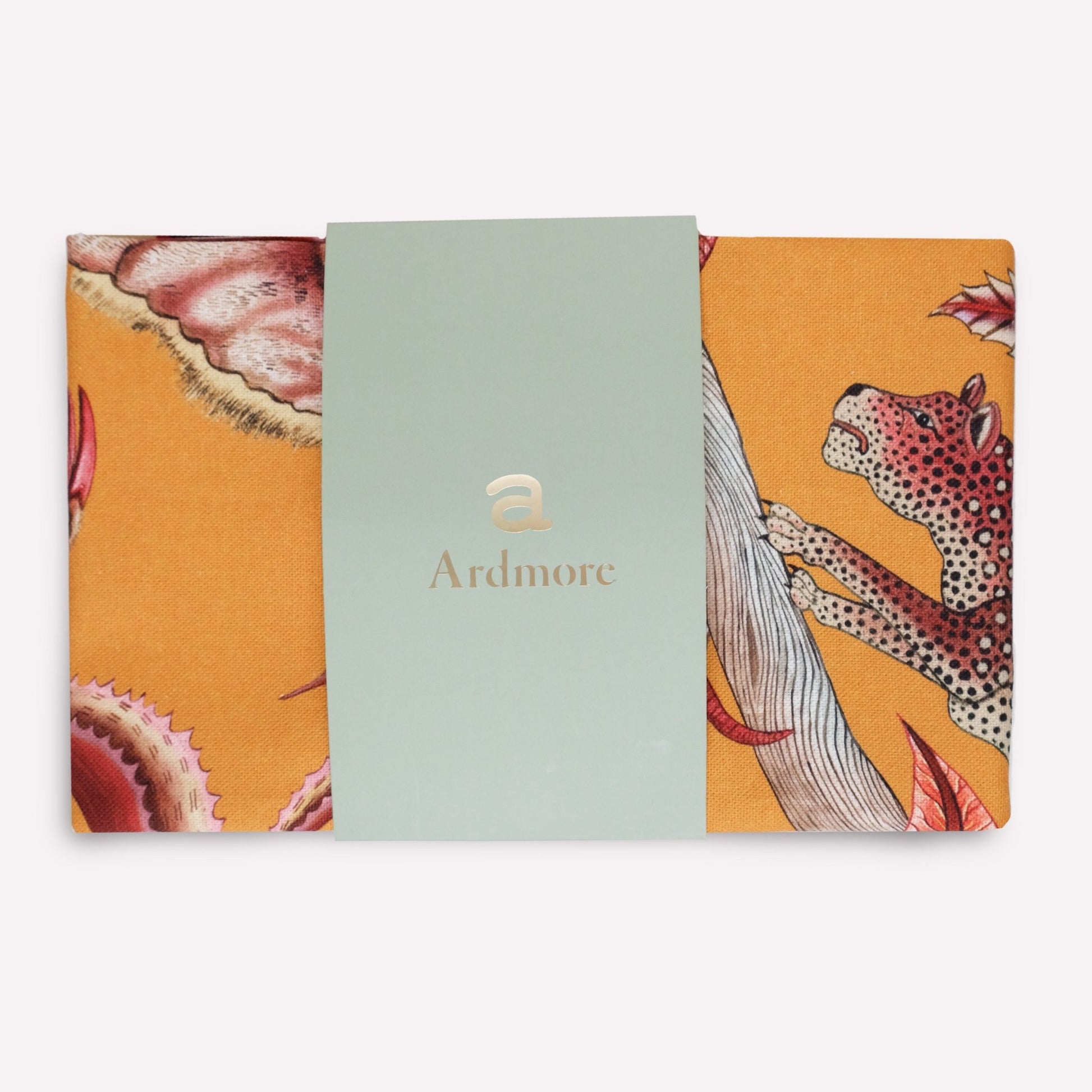 A tea towel in its original packaging, displaying the mix of botanical elements and safari animals in a sophisticated warm-toned theme.