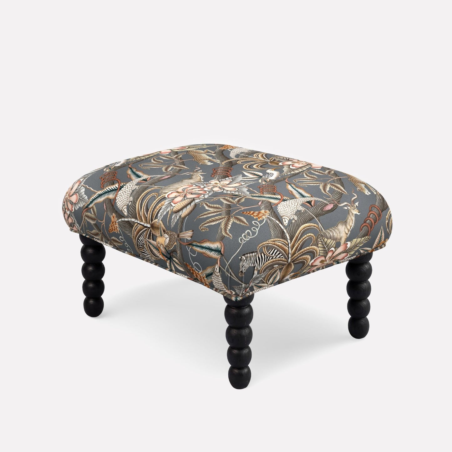 Ardmore Kudu Pod Ottoman upholstered in Pangolin Park Ash Linen, featuring a dark botanical fabric with intricate patterns and sculpted black spindle legs.