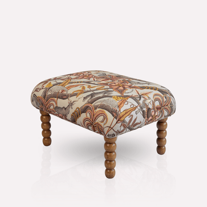 Side view of the Ardmore Kudu Pod Ottoman, showcasing its rich fabric design and finely crafted wooden legs.