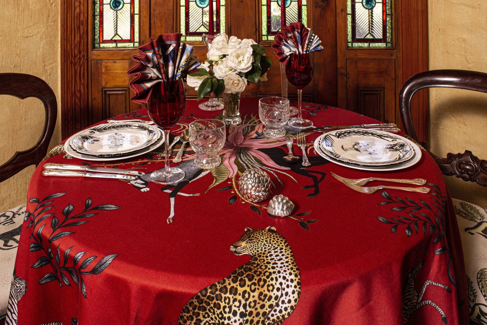 An overhead perspective of a beautifully set dining table featuring the Leopard Lily Square Tablecloth in Royal Red, highlighting its symmetrical design and opulent detailing.