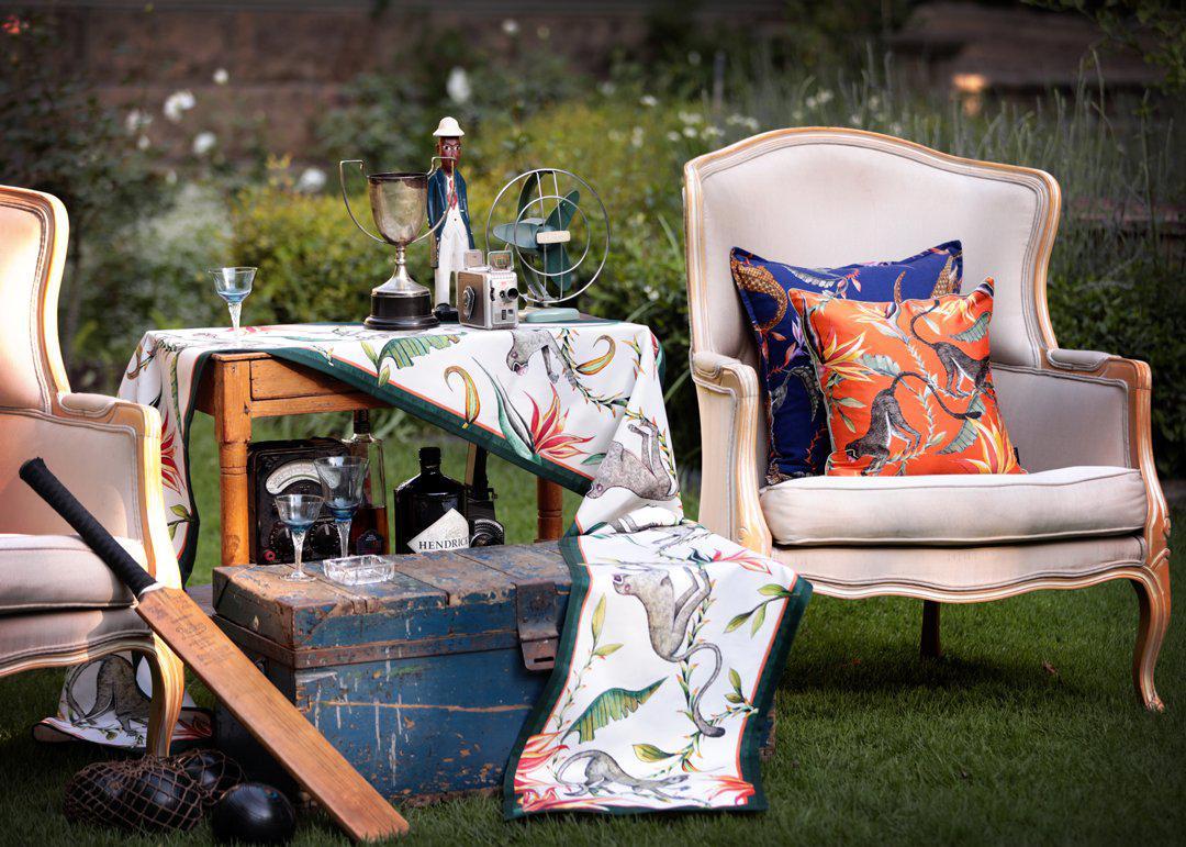 Lifestyle image of the River Chase Royal Linen cushion cover placed on an outdoor chair, styled with a matching table runner for a sophisticated setting.