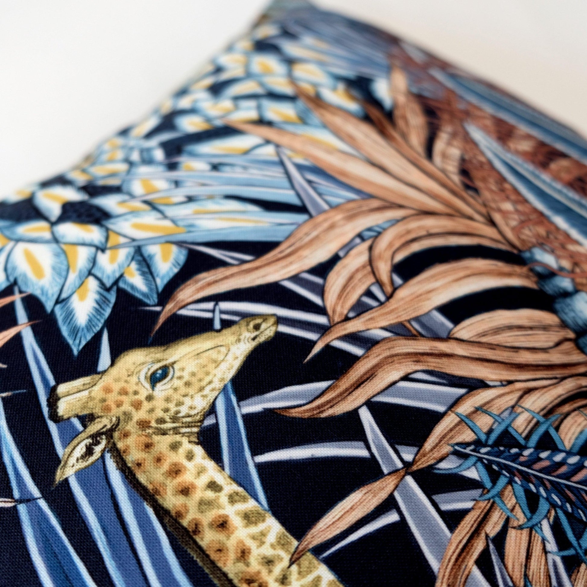 Close-up of the Sabie Forest Dawn cushion cover, focusing on the delicate depiction of a giraffe amid detailed leaves and flowers in blue and beige tones.