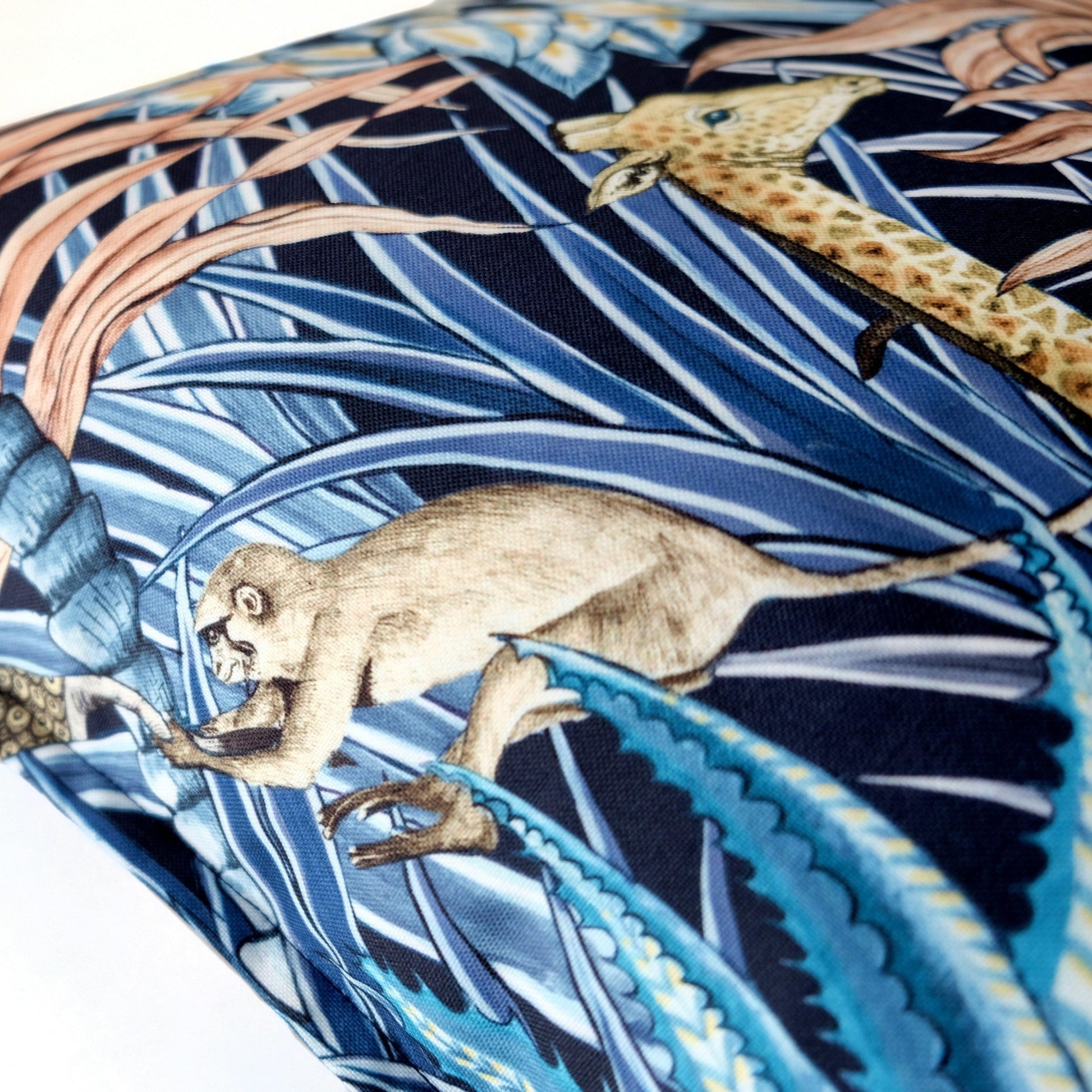 Detailed close-up of the Sabie Forest Dawn cushion cover, highlighting a small animal motif, possibly a mongoose, among tropical plants on a dark blue background.