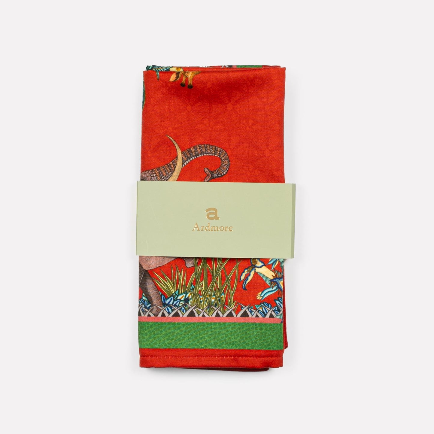 A neatly folded Ardmore Sabie Forest Napkin in Royal Red, wrapped in its branded packaging, emphasizing its premium cotton material and vibrant digital print.