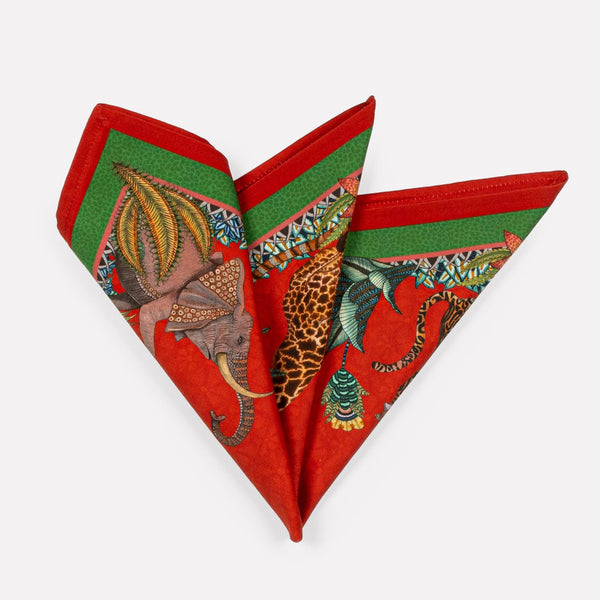 A pair of Ardmore Sabie Forest Napkins in Royal Red, folded into a fan shape, showcasing a vibrant red background with lush green foliage and a detailed leopard illustration.