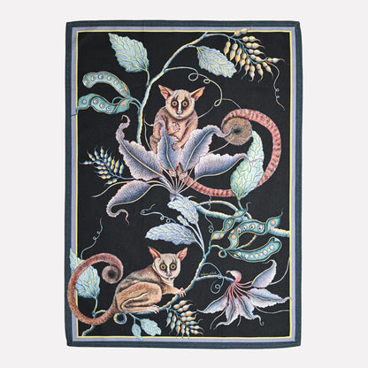 A luxurious tea towel featuring an intricate nighttime scene of bush babies and exotic foliage, set against a deep black background with elegant pastel details.