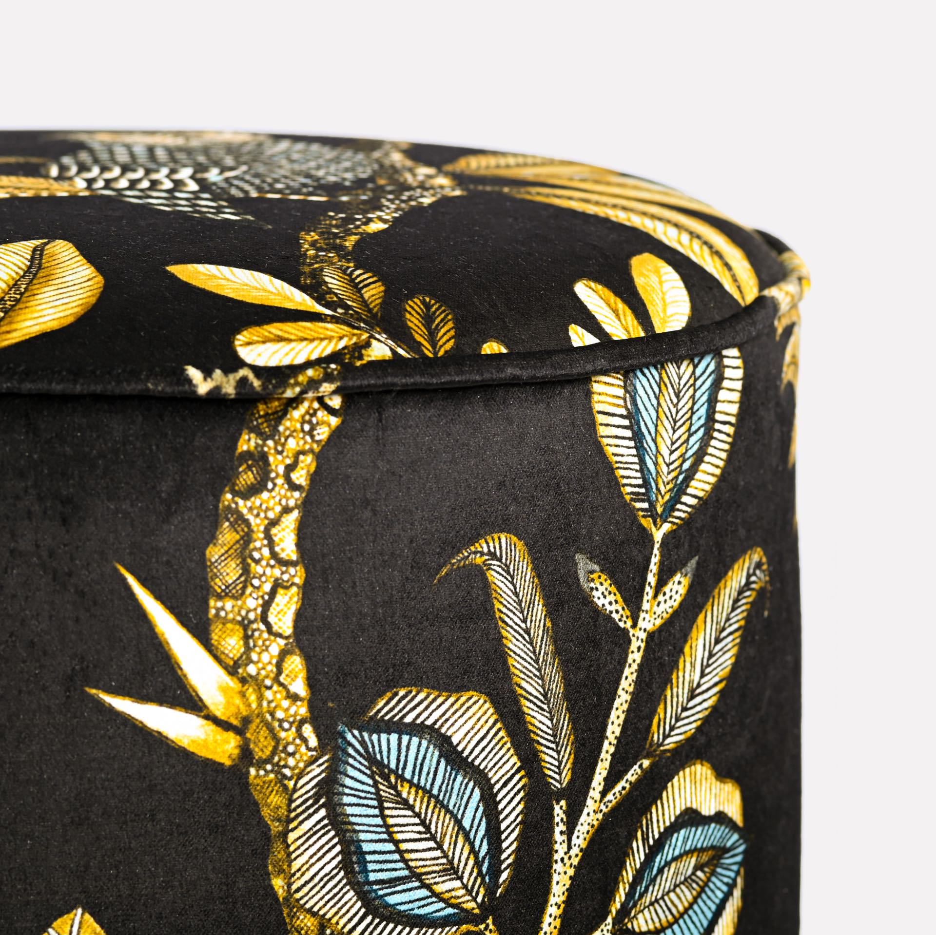 Side close-up of the Ardmore Camp Critter Brass Velvet Pouffe, highlighting the luxurious texture of the fabric and the detailed golden embroidery of African-inspired wildlife patterns.