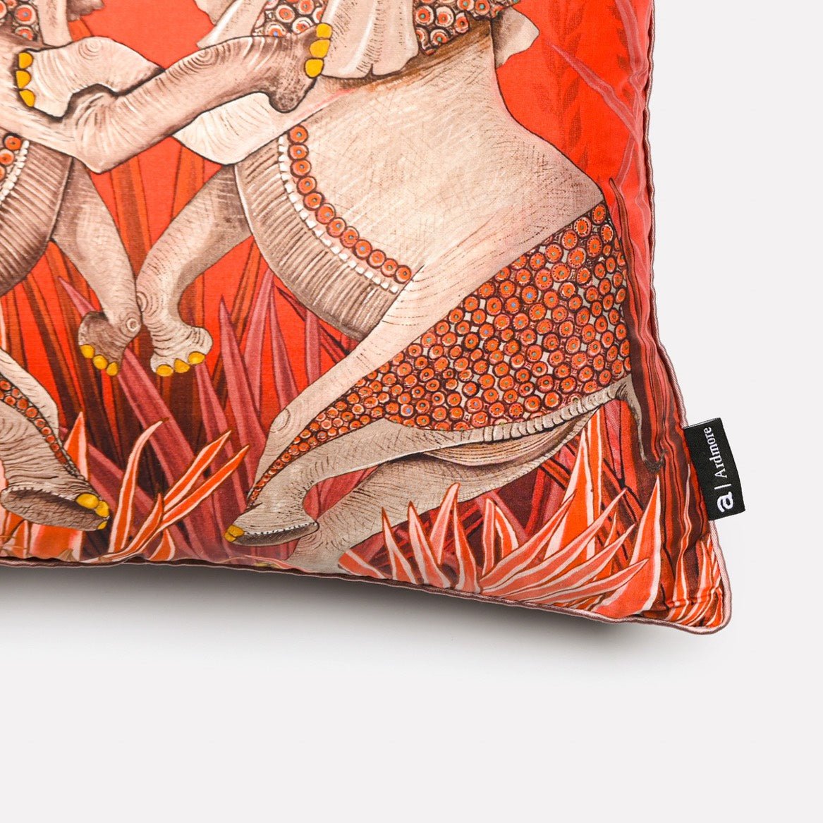 Angled close-up of the Dancing Elephant Sunset silk cushion cover, highlighting the detailed patterns of the elephants and the rich orange and pink tones of the luxurious silk fabric.