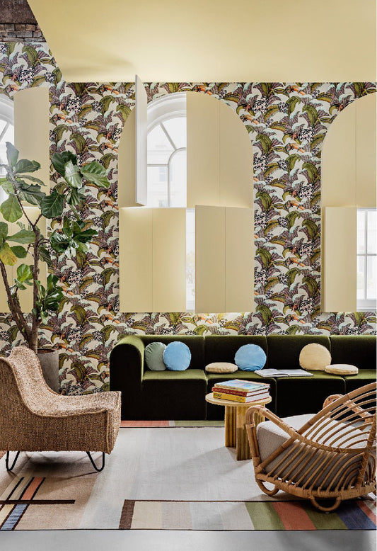 A beautifully styled room with high arched windows, featuring the wallpaper’s lush foliage, exotic birds, and intricate patterns, evoking a sense of tropical elegance.