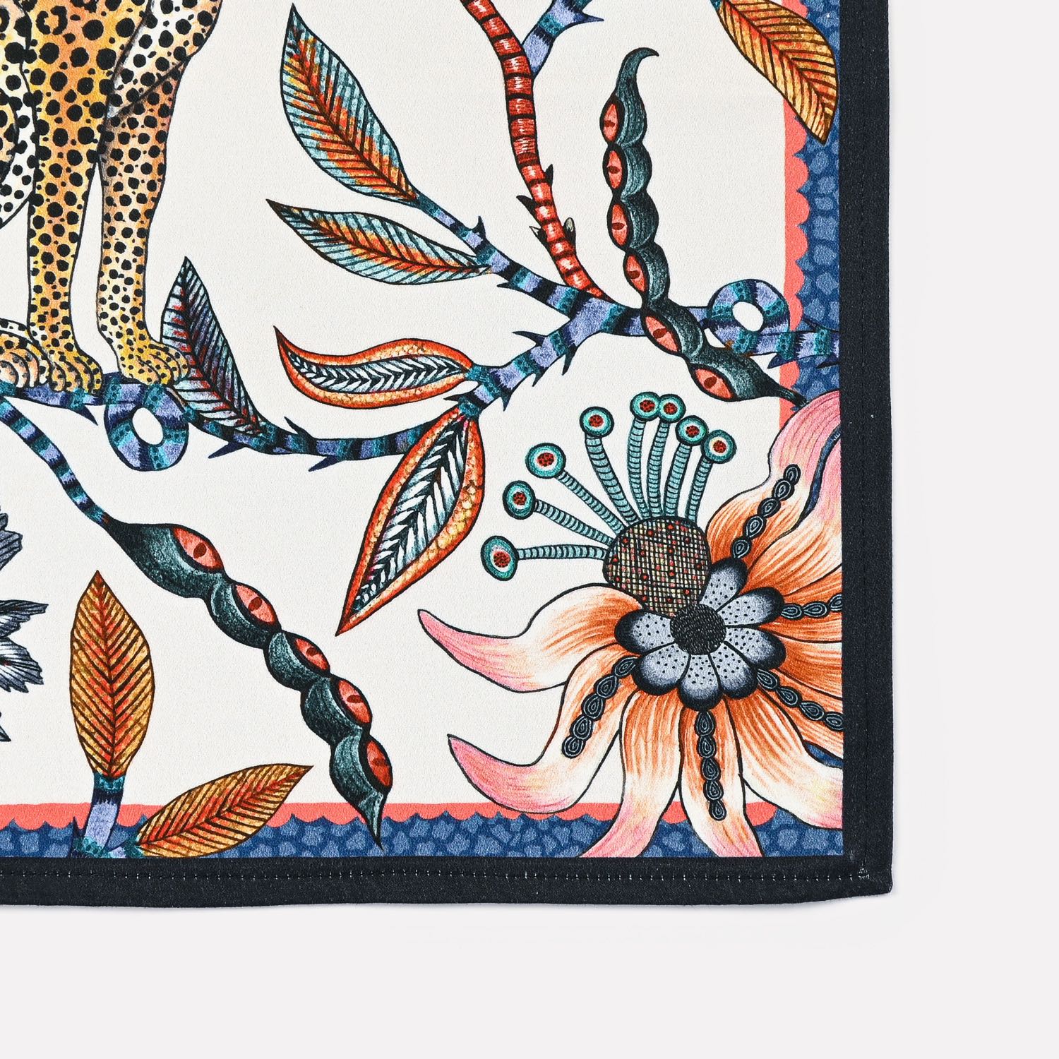 A close-up of the Ardmore Leopard Napkin in Frost, emphasizing the floral accents, delicate leaves, and rich navy border in a balanced composition.