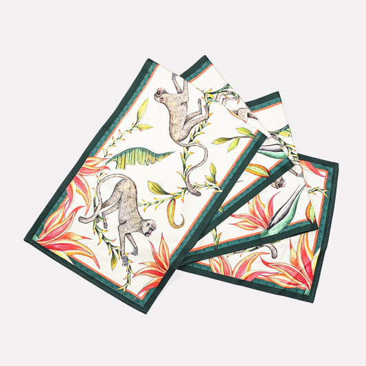 A set of Ardmore's Monkey Paradise table runners in a soft Chalk hue, featuring intricately illustrated leopards, jackals, and lush foliage.