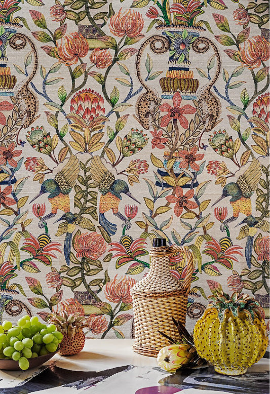 A vibrant display of the wallpaper featuring the King Protea, sunbirds, and chameleons in a warm coral pink and red palette, styled with decorative kitchenware.