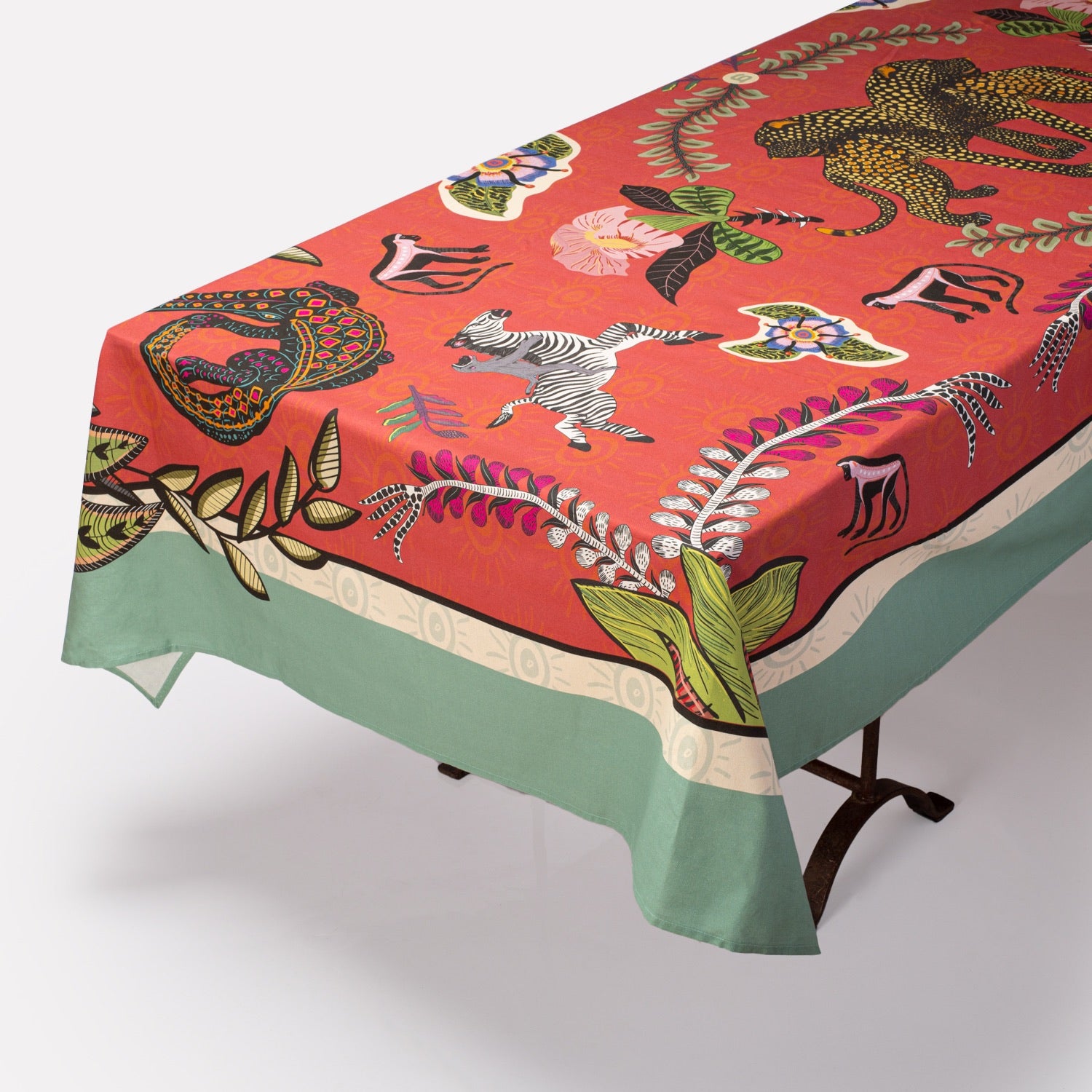 The Royal Leopard Tablecloth in Sunset elegantly draped over a dining table, showing its vibrant red colour and detailed safari-inspired illustrations.