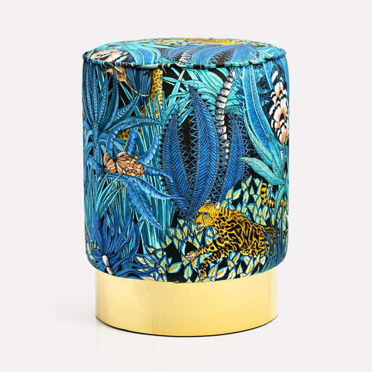 Luxurious velvet pouffe featuring Ardmore's Sabie Forest Tanzanite design, showcasing a vivid blue jungle-inspired pattern with golden accents, set atop an elegant brass base.