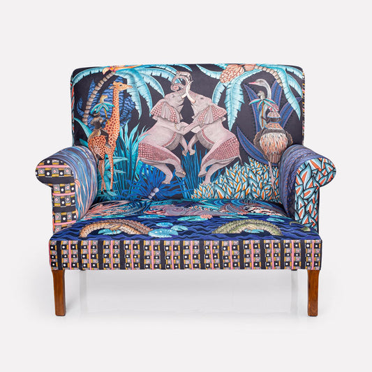 A full-frontal view of the Ardmore Sabie Sofa in Tanzanite, showcasing its intricate design featuring elephants, a juggling monkey, and vibrant flora.